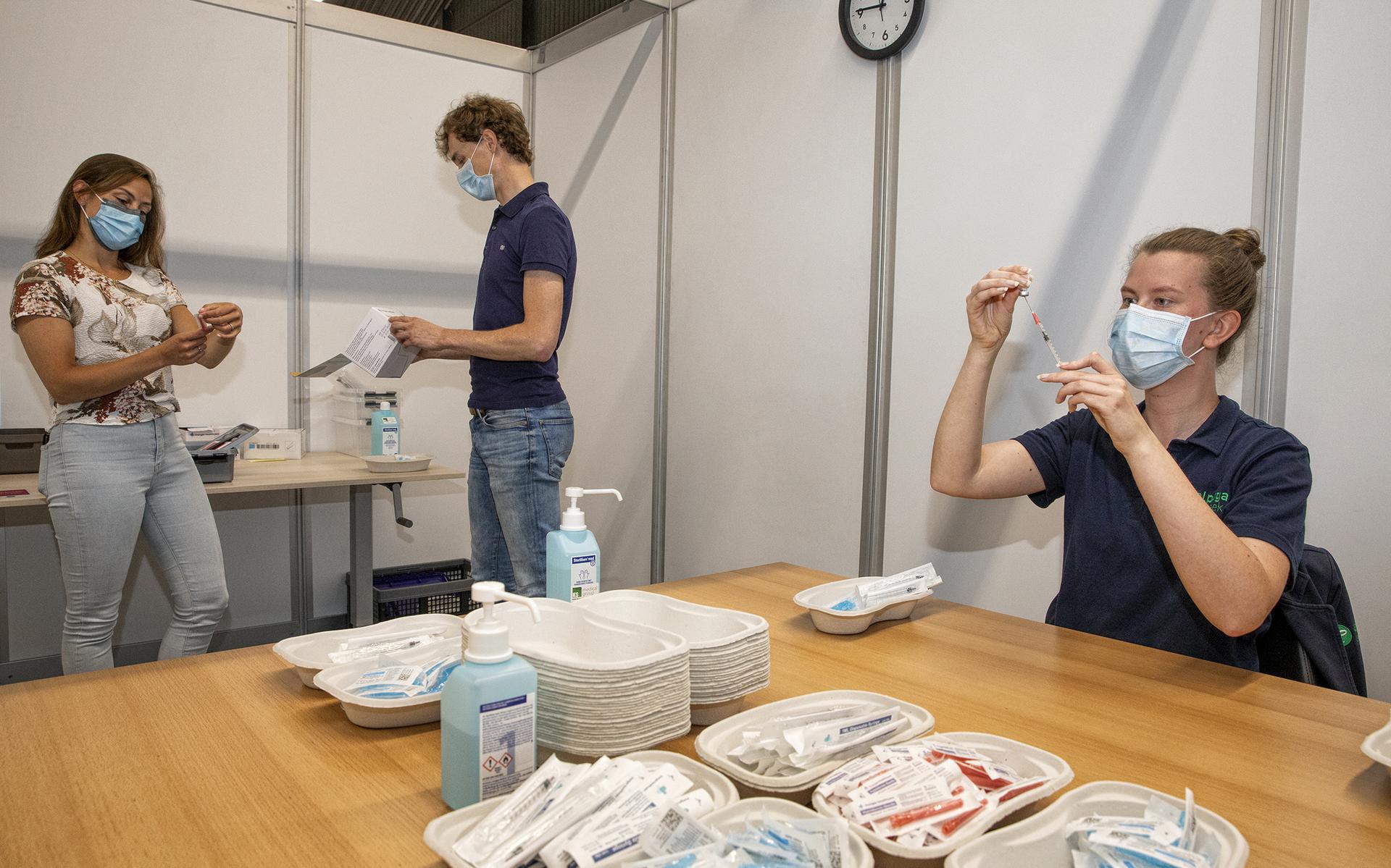 Kyra Esméé Zwart is op de vaccinatielocatie in Appelscha bezig met het gereedmaken van de spuiten. Op de achtergrond hebben Rogier Hilbers en Maxime Tjioe overleg met elkaar.